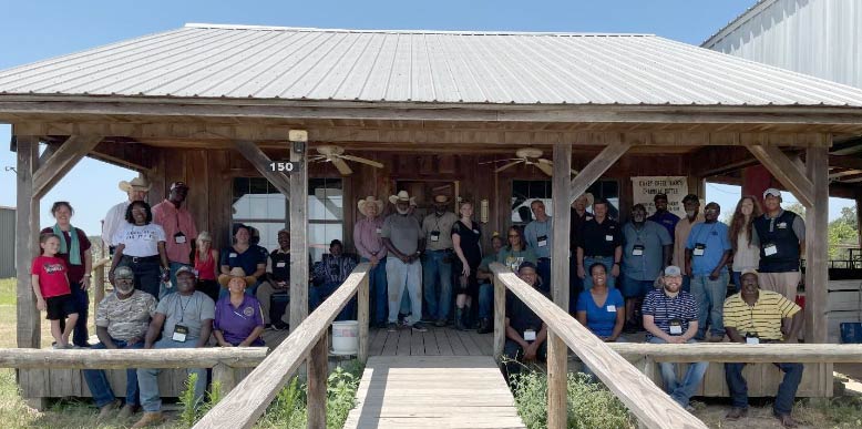 A group of about 30 people are gathered on the covered porch of a farm building. They